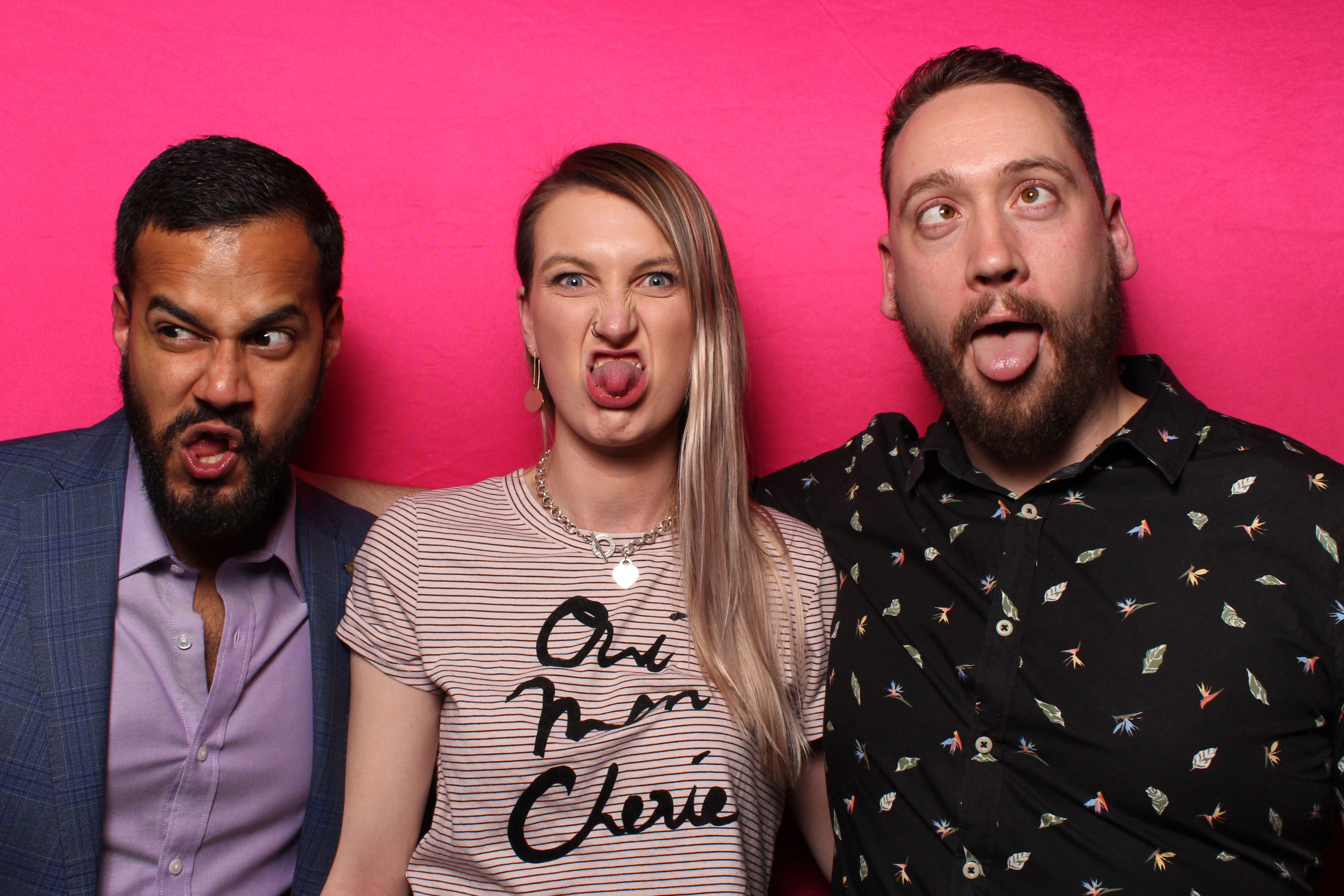 Three people pulling faces infront of a pink backdrop